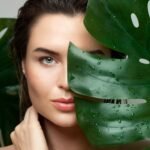 Close up of clear, hydrated skin beside a large green monstera leaf